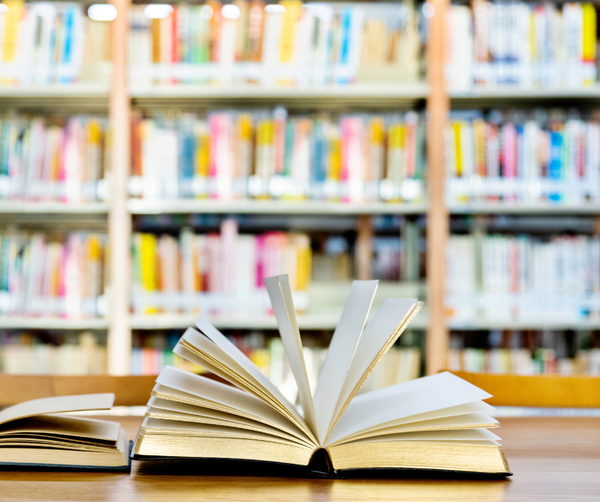 Image of an open book on a table with library bookshelves in the background